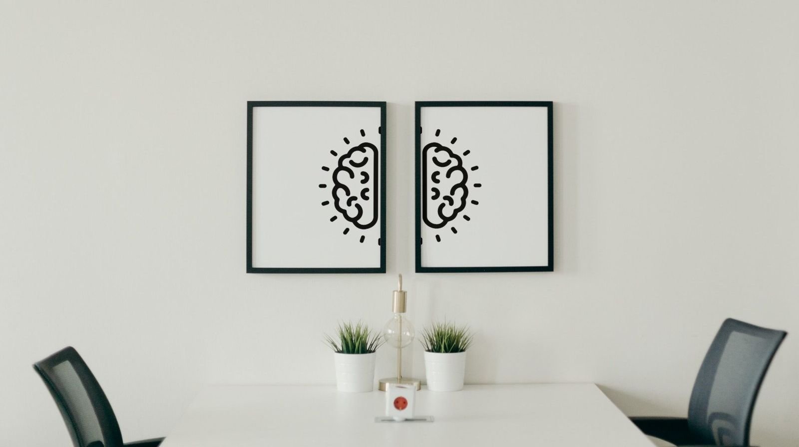 Two framed prints on a white wall, each showing one half of the Thrivology brain mark