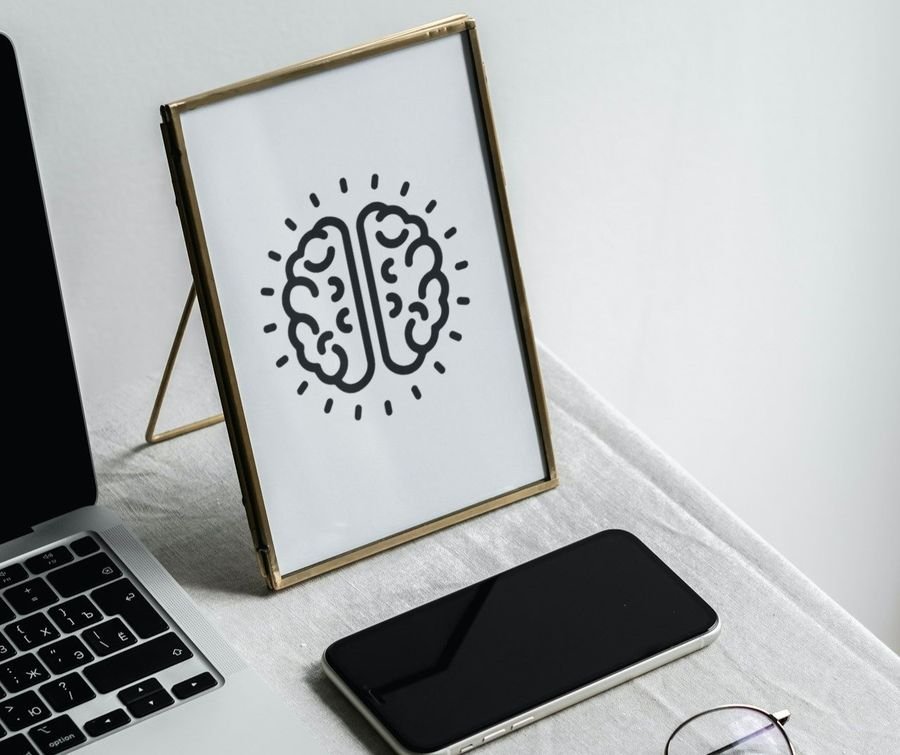 The brain mark in a brass frame on a linen-covered desk beside a laptop