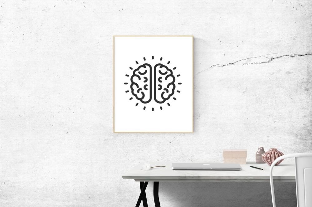 The brain mark in a light wood frame above a white desk and a closed laptop