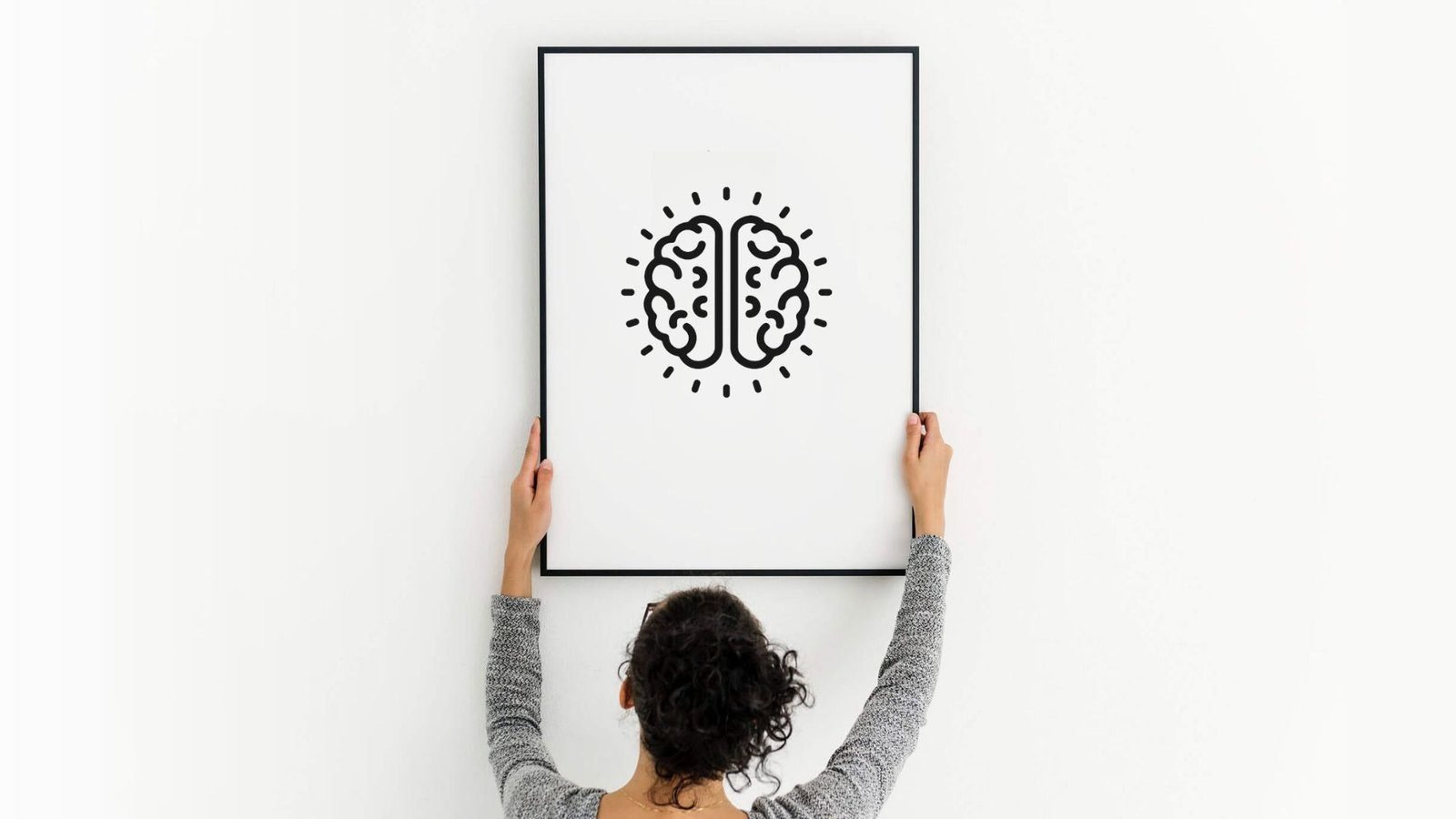 A person hangs a large framed print of the Thrivology brain mark on a white wall